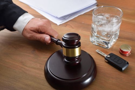 Gavel on a desk with a glass of alcohol and car keys